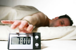 photo of man htting snooze button on alarm clock